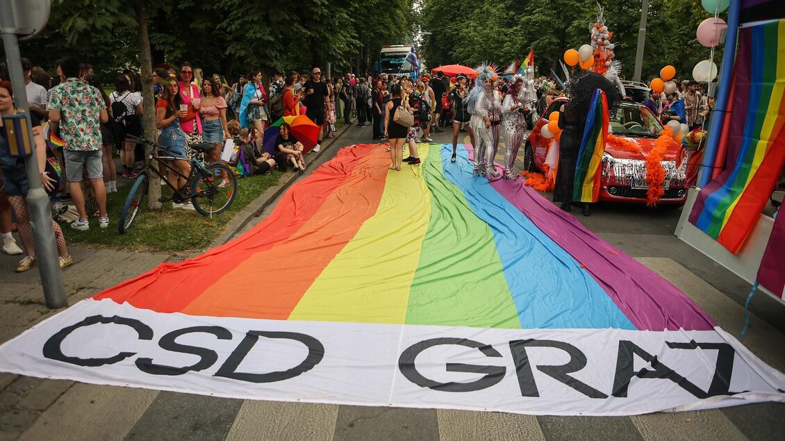 Eine bunte Parade zum Christopher Street Day mit einem großen Regenbogenbanner. Viele Menschen feiern und tragen farbenfrohe Kleidung. | © @Seabstian Neugebauer