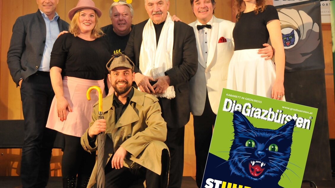 Eine Gruppe von sieben Personen in festlicher Kleidung posiert lächelnd für die Kamera. Im Vordergrund hält jemand eine Lupe und es gibt eine Zeitschrift mit einer Katze auf dem Titel. | © RETTER Bio- Natur- Resort