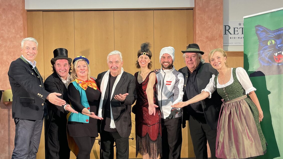 Eine Gruppe von acht Personen steht zusammen auf einer Bühne. Sie tragen verschiedene Kostüme und lächeln in die Kamera. | © ****Retter Bio-Natur-Resort