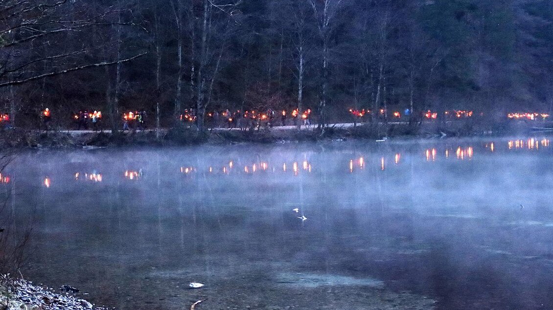 Ein ruhiger See mit sanftem Nebel und schimmernden Lichtern am Ufer. Die Bäume im Hintergrund schaffen eine mystische Atmosphäre. | © Naturfreunde Eisenerz