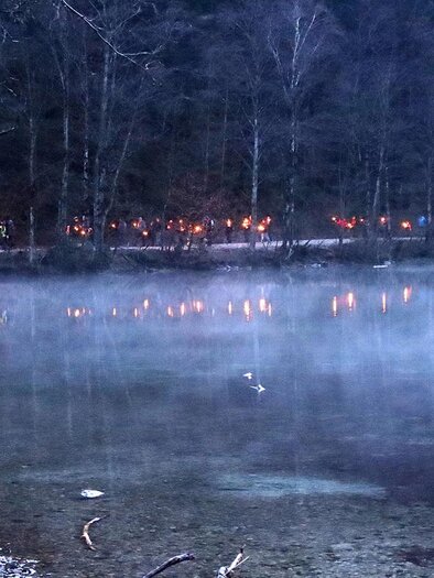 A tranquil lake with soft fog and shimmering lights on the shore. The trees in the background create a mystical atmosphere. | © Naturfreunde Eisenerz