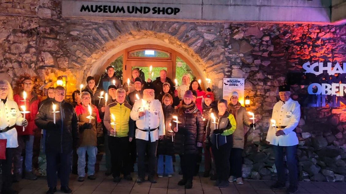 Eine Gruppe von Menschen steht vor einem Gebäude mit Fackeln in der Hand. Das Licht des Gebäudes sorgt für eine festliche Atmosphäre. | © Hannes Pfandl