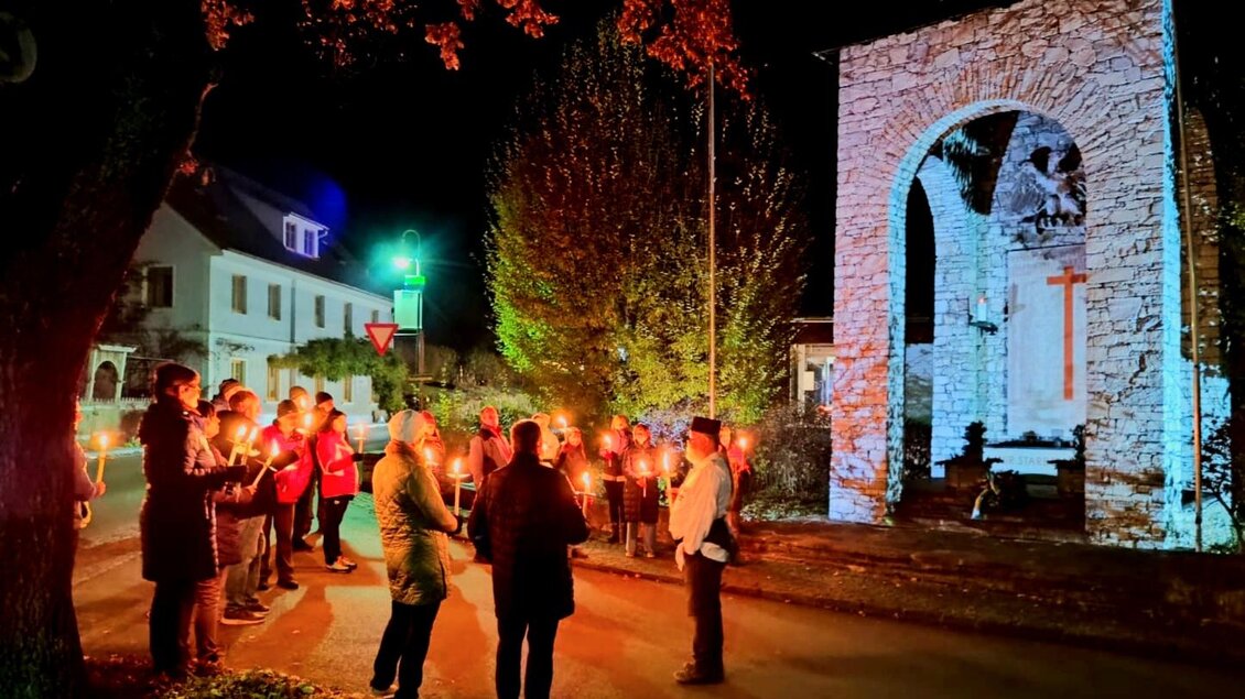Eine Gruppe von Menschen steht bei Nacht vor einem beleuchteten Tor. Sie halten Kerzen in der Hand und scheinen an einer Zeremonie oder Veranstaltung teilzunehmen. | © Hannes Pfandl