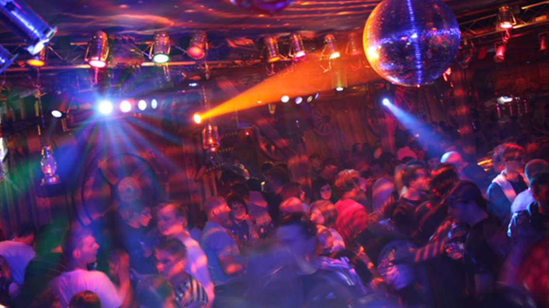 Ein belebter Club mit bunter Beleuchtung und einer Discokugel. Viele Menschen tanzen und genießen die Musik. | © Toms Stadl