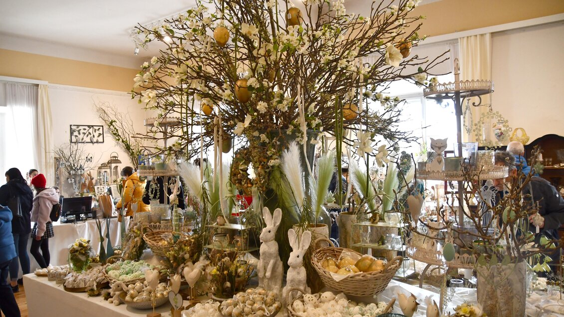 Ein festlich dekorierter Tisch mit einem großen Baum, geschmückt mit Eiern und Blumen. Rundherum befinden sich verschiedene österliche Dekorationen und Geschäfte. | © Thermen- & Vulkanland