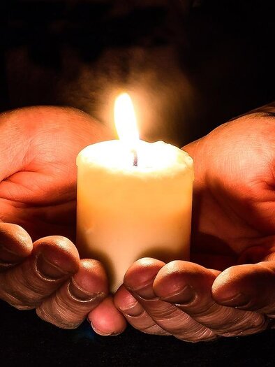 Two hands hold a burning candle. The warm glow of the candle illuminates the darkness. | © pixabay.com