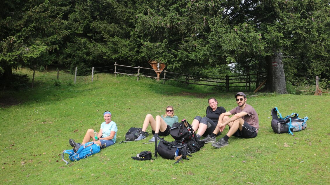 Vier Wandernde machen Rast auf einer Wiese am Walzkogel, umgeben von Rucksäcken am Rand des Nadelwaldes. | © Heinz Kaltschmidt