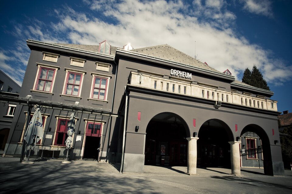 Ein historisches Gebäude mit der Aufschrift "Orpheum" an der Fassade. Die Struktur hat einen eleganten architektonischen Stil und wird von einem blauen Himmel umrahmt. | © (c) Spielstätten - Lupi Spuma
