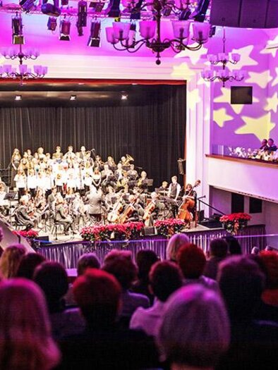 A concert hall with an orchestra on stage. Many spectators are sitting and enjoying the performance under colorful lights. | © Stadt Bruck an der Mur