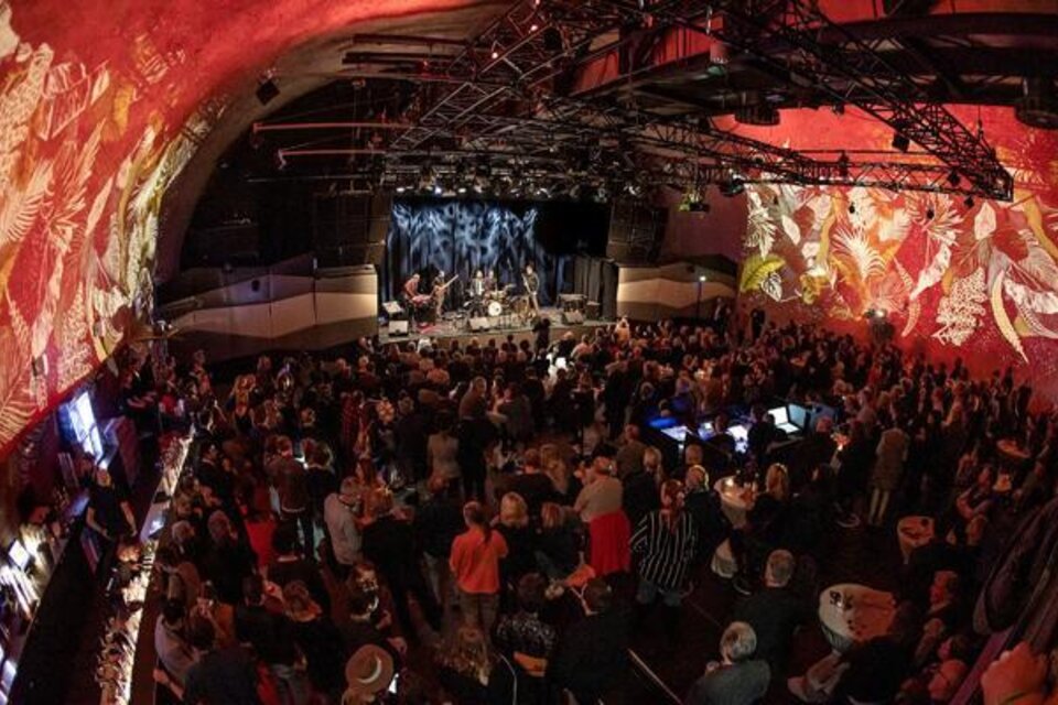 Eine lebhafte Veranstaltung in einem gut besuchten Veranstaltungsort mit bunten Wandmalereien. Die Band spielt auf der Bühne, während das Publikum begeistert zuschaut. | © Jazz REdoute.