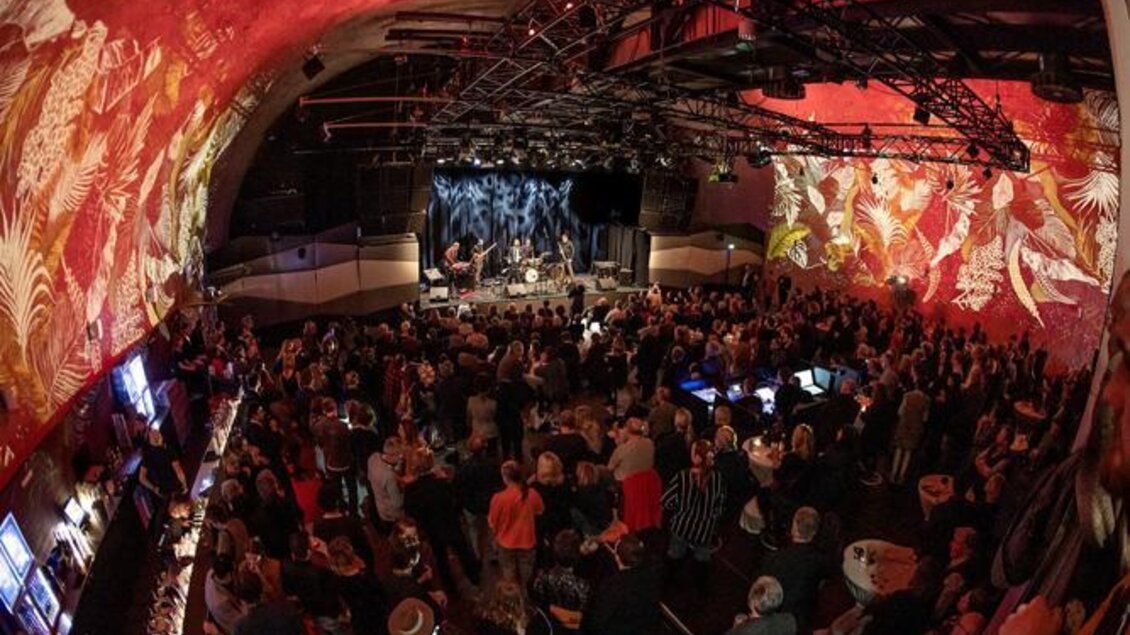 Eine lebhafte Veranstaltung in einem gut besuchten Veranstaltungsort mit bunten Wandmalereien. Die Band spielt auf der Bühne, während das Publikum begeistert zuschaut. | © Jazz REdoute.