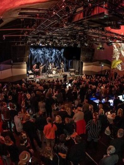 Eine lebhafte Veranstaltung in einem gut besuchten Veranstaltungsort mit bunten Wandmalereien. Die Band spielt auf der Bühne, während das Publikum begeistert zuschaut. | © Jazz REdoute.