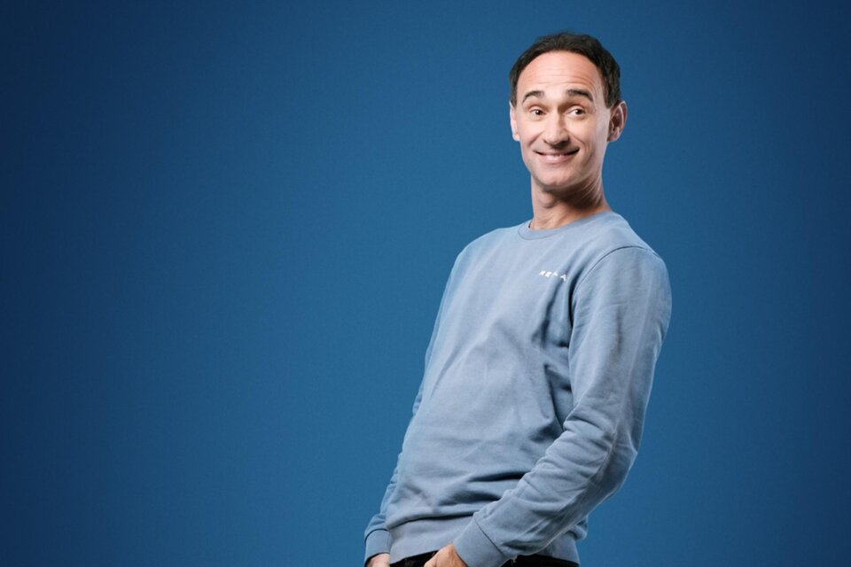 Porträt von Gernot Kulis, einem österreichischen Komiker, der in einem blauen Sweatshirt vor einem blauen Hintergrund steht. In einer entspannten Pose lächelt er charmant in die Kamera. | © Hans Leitner