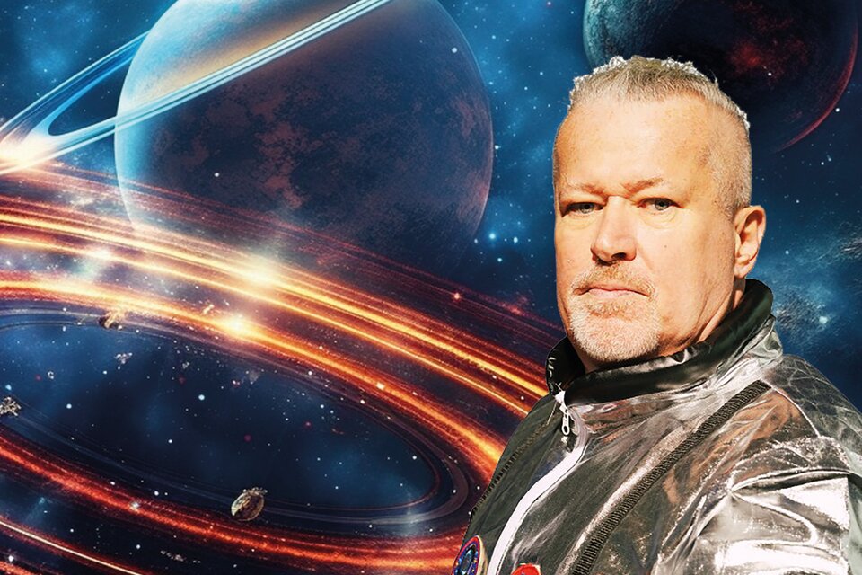 Mike Supancic trägt einen glänzenden, silbernen Raumanzug mit Emblemen, während er vor einem farbenprächtigen, galaktischen Hintergrund mit Planeten und Ringen steht. Der Bildausschnitt vermittelt eine Szene aus dem Weltraum, die mit futuristischem Flair und einer kosmischen Atmosphäre gestaltet ist. | © Lukas Beck