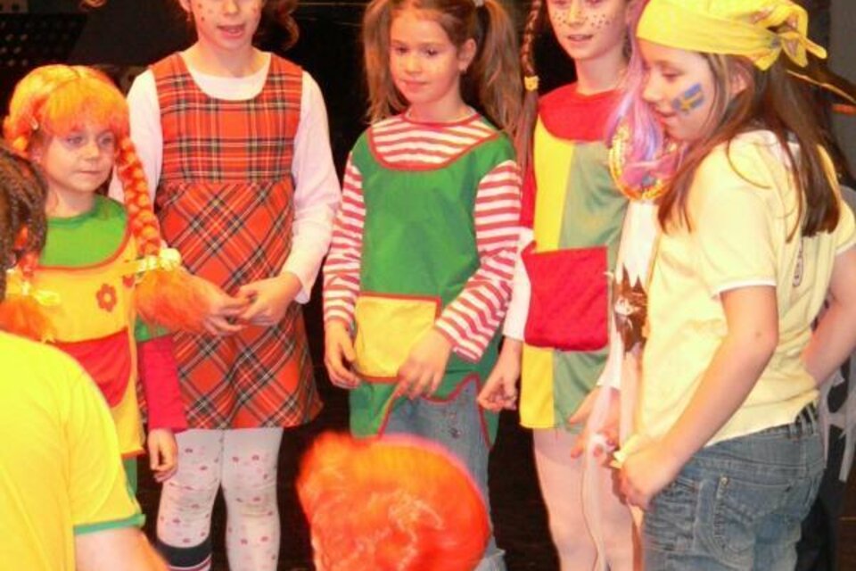 Eine Gruppe von Mädchen in bunten Kostümen steht zusammen auf einer Bühne. Sie haben fröhliche Gesichtsmalerei und zeigen viel Spaß. | © Lederer