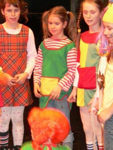 A group of girls in colorful costumes is standing together on a stage. They have cheerful face painting and show a lot of fun. | © Lederer