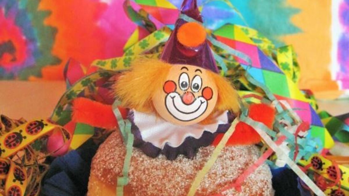 Ein bunter Krapfen mit einer Clownfigur und Konfetti. Der Hintergrund ist farbenfroh und festlich. | © Lederer
