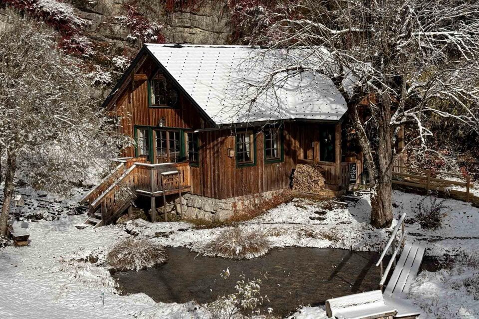 Ein charmantes, holzverkleidetes Haus in einer schneebedeckten Landschaft. Drumherum sind kahle Bäume und ein kleiner Teich sichtbar. | © Cafe Viola, Marina Schobegger