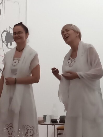 Zwei Sängerinnen in weißen Kleidern singen in einem Raum mit großen Bildern an der Wand.  | © Oswald Schechtner