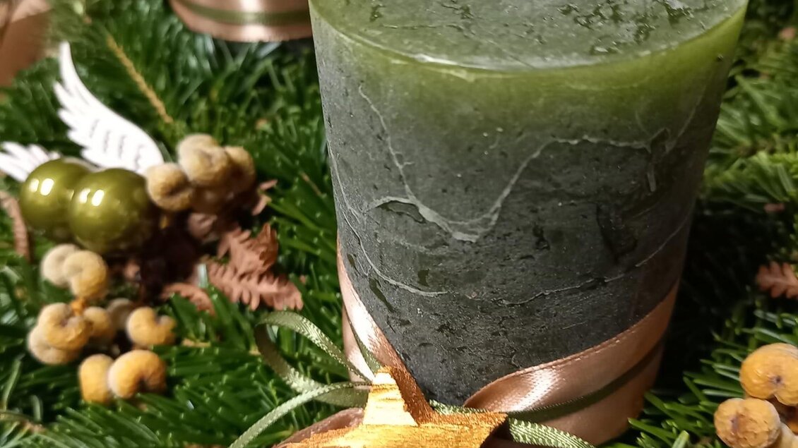 Eine grüne Kerze steht auf einem schönen Adventskranz mit Tannenzweigen und goldenen Verzierungen. Der Kranz ist festlich dekoriert und vermittelt eine gemütliche Atmosphäre. | © Blumenhof Bender