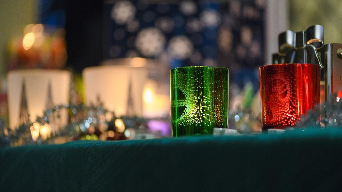 Bunte Kerzen in grünen und roten Farben stehen auf einem Tisch. Im Hintergrund sind weitere dekorative Elemente erkennbar. | © Waltraud Eberhart