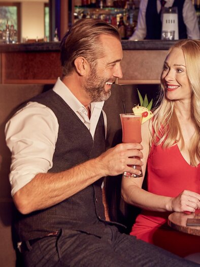 Ein Paar sitzt in einer Bar und genießt farbenfrohe Cocktails. Sie lächeln sich an und scheinen eine entspannte Zeit zu haben. | © Hotel Stoiser