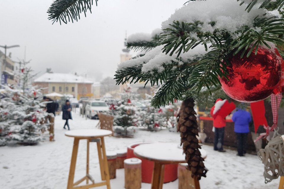 Ein verschneiter Weihnachtsmarkt mit Tannenbäumen und festlicher Dekoration. Menschen schlendern durch die winterliche Atmosphäre. | © Stadt Mürzzuschlag, Bettina Rinnhofer