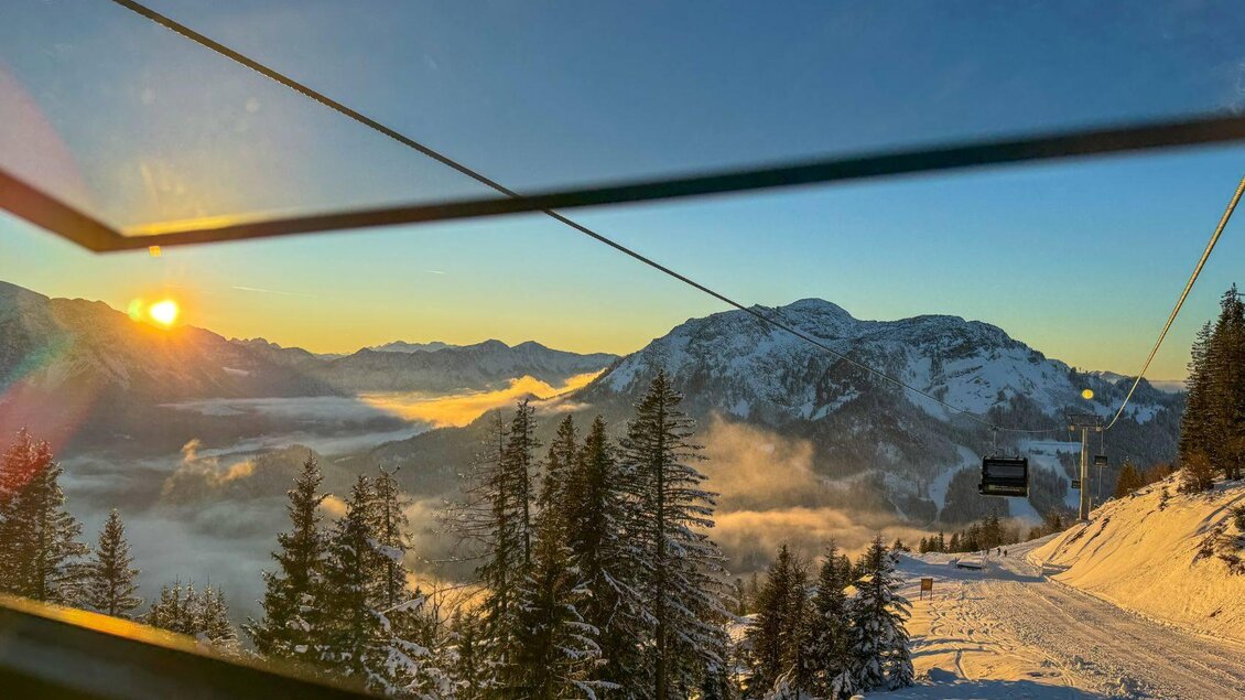 Eine winterliche Berglandschaft mit schneebedeckten Bergen und einer strahlenden Sonne am Horizont. Im Vordergrund stehen verschneite Bäume und eine Skipiste. | © Theresa Schwaiger_TVB Ausseerland Salzkammergut