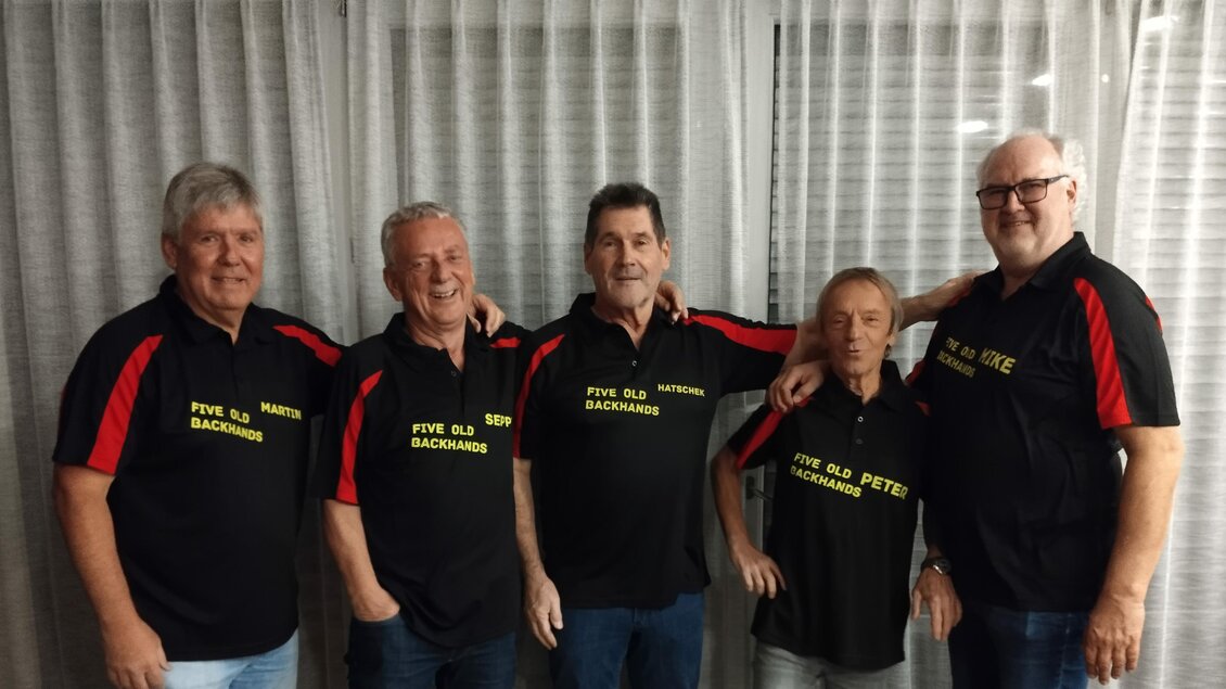 Fünf Männer stehen nebeneinander und tragen schwarze Poloshirts mit roten Akzenten. Die Shirts haben Aufdrucke in Gelb. | © Peter Raffler