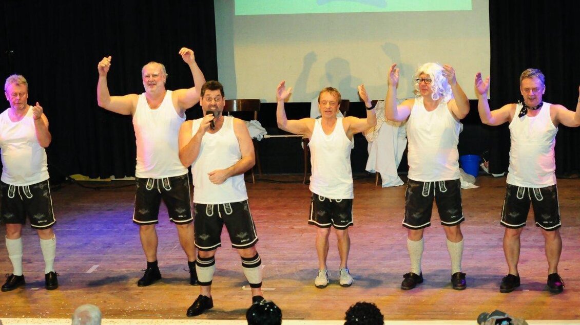 Eine Gruppe von Männern steht auf der Bühne und trägt sportliche Kleidung. Sie zeigen eine unterhaltsame Darbietung und posieren fröhlich für das Publikum. | © Werner Friedl