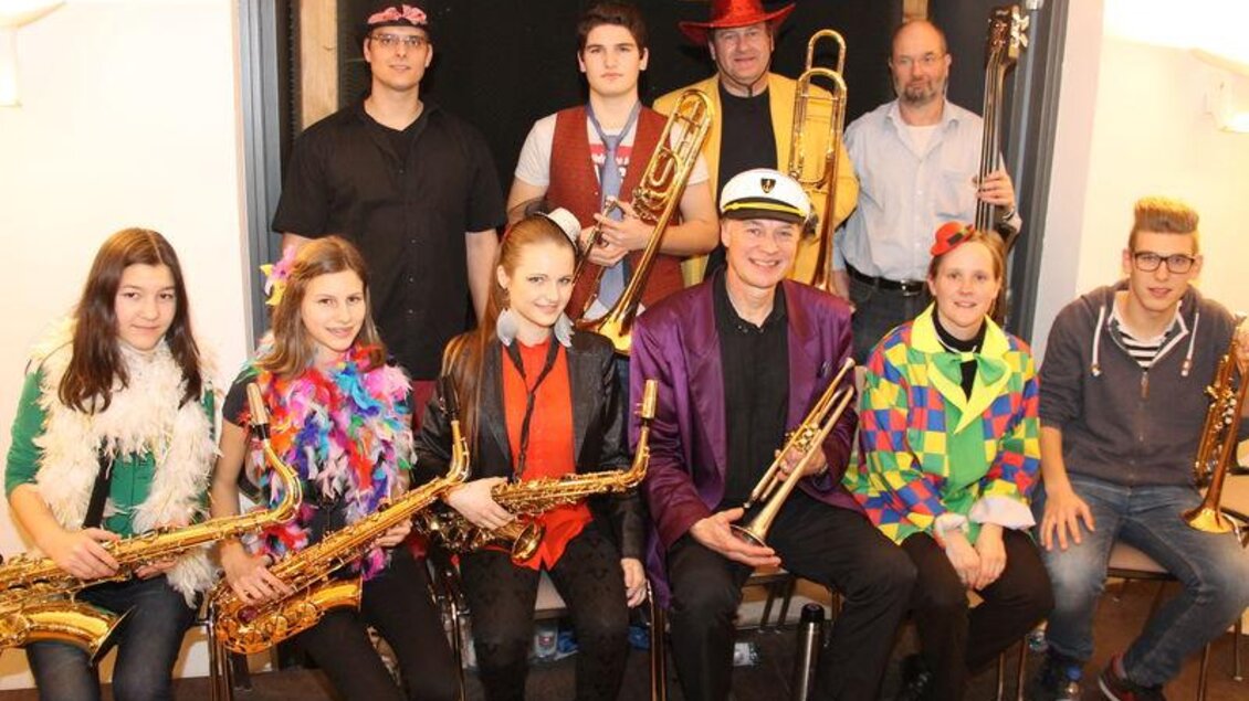 Eine Gruppe von Musikern steht und sitzt zusammen und spielt verschiedene Blasinstrumente. Die Künstler tragen bunte Kostüme und haben viel Spaß.