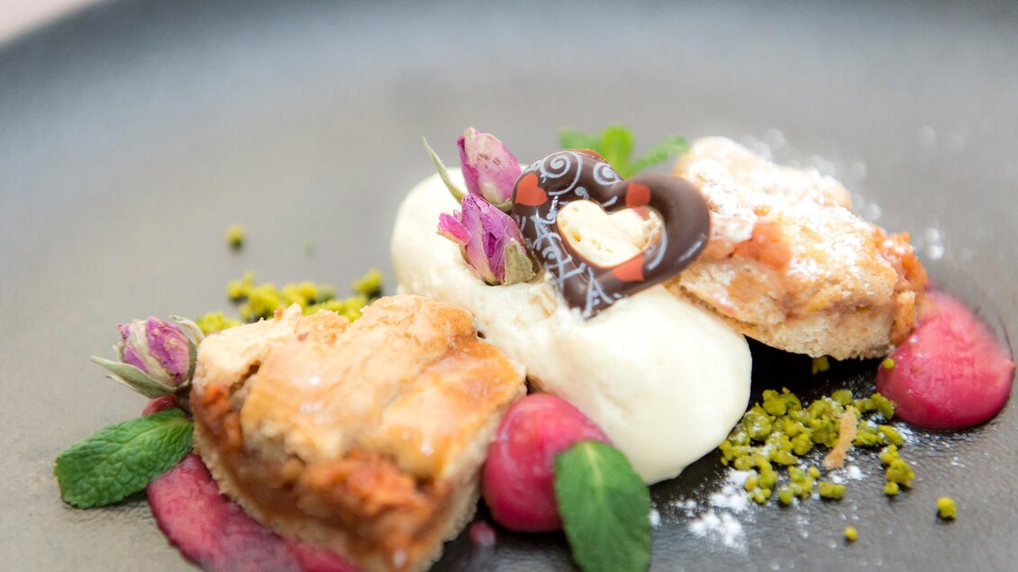 Ein kunstvoll angerichteter Dessertteller mit einer Kombination aus Biskuit, Eiscreme und Früchten. Dekoriert mit essbaren Blüten und Schokoladenelementen. | © RETTER- BIO- Natur- Resort