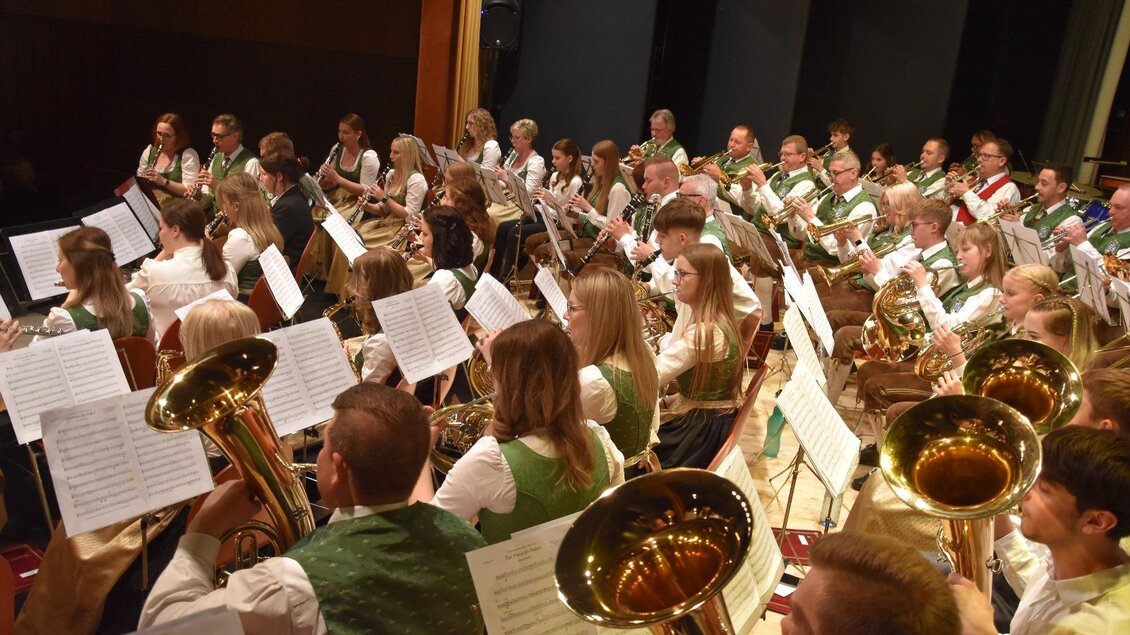 Eine große Blaskapelle spielt auf der Bühne. Die Musiker tragen traditionelle Kleidung und haben Notenblätter vor sich. | © MMK Bad Waltersdorf