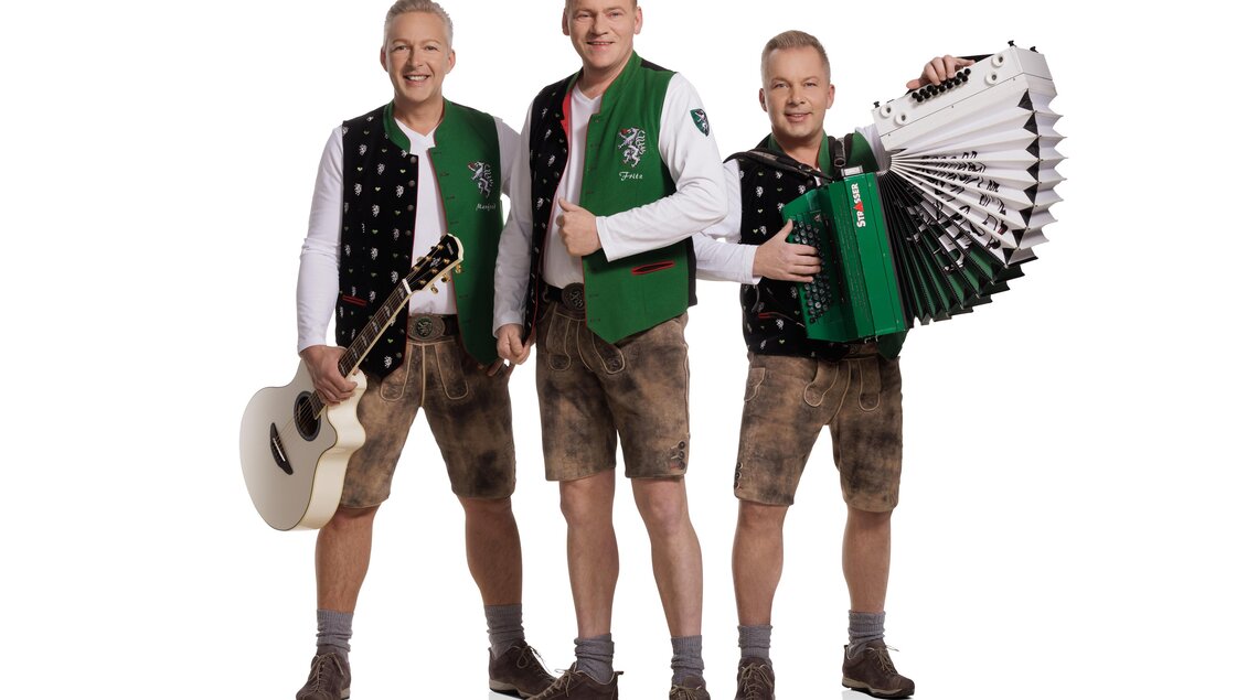 Drei Männer in traditioneller bayerischer Tracht stehen nebeneinander. Einer hält eine Gitarre, ein anderer ein Akkordeon, und sie lächeln freundlich. | © DIE EDLSEER_KarlSchrotter