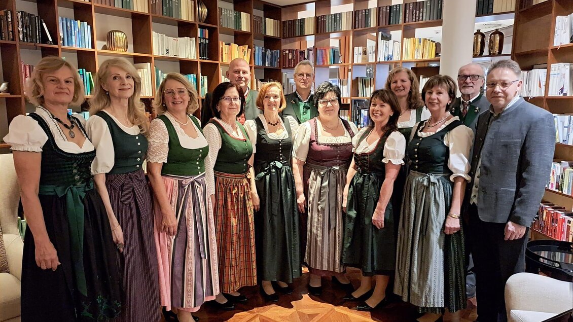 Eine Gruppe von Menschen, die traditionelle Trachten trägt, steht in einem Raum mit Bücherregalen. Die Atmosphäre wirkt festlich und einladend. | © Singkreis Bad Waltersdorf