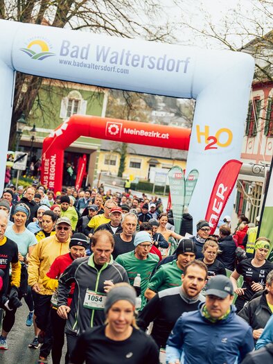 A group of runners is starting at a race in Bad Waltersdorf. Colorful sportswear and a large starting arch characterize the scene. | © Hikimus