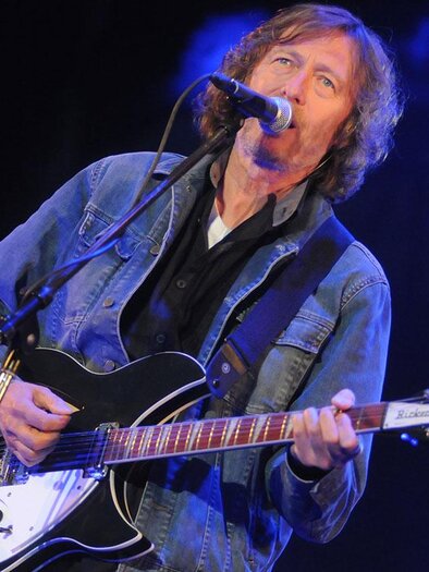 Ein Musiker spielt Gitarre auf der Bühne. Er trägt eine Jeansjacke und hat lange, lockige Haare. | © didilipkovich