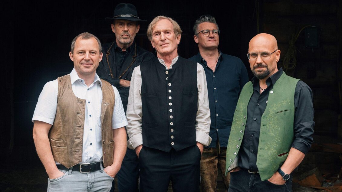 Fünf Männer in traditioneller Kleidung stehen zusammen. Sie haben unterschiedliche Outfits, darunter Westen und Hüte, und schauen in die Kamera. | © Karl Steinegger