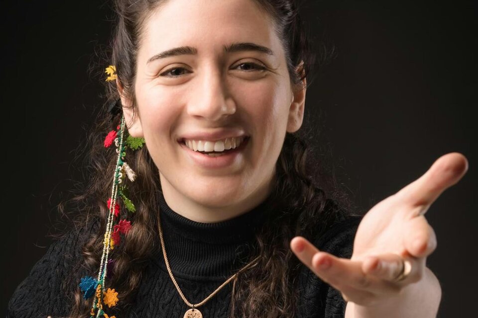 Die Dirigentin Nil Venditti hat zwei bunte Bänder im Haar, sie lächelt und streckt den linken Arm entgegen.  | © Alessandro Bartani