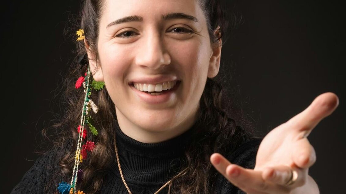 Die Dirigentin Nil Venditti hat zwei bunte Bänder im Haar, sie lächelt und streckt den linken Arm entgegen.  | © Alessandro Bartani