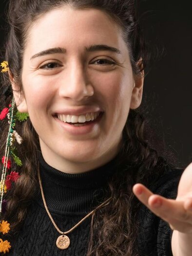 The conductor Nil Venditti has two colorful ribbons in her hair, she smiles and extends her left arm. | © Alessandro Bartani