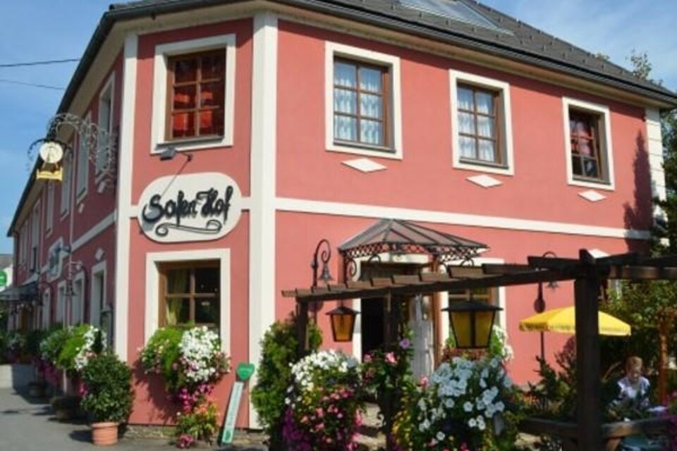 Ein hübsches, rosa Gebäude mit dem Namen "Sofitel". Blumenkästen und eine sonnige Atmosphäre schaffen eine einladende Stimmung.