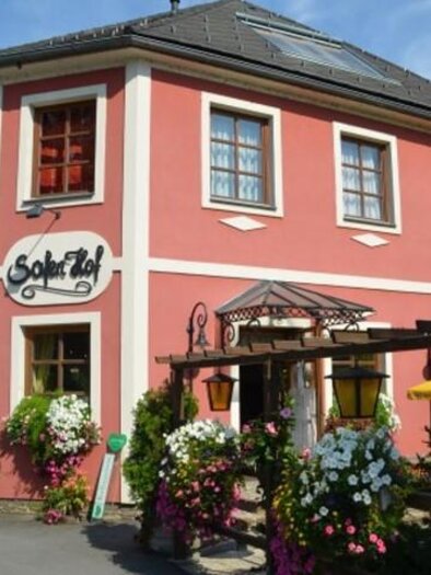 Ein hübsches, rosa Gebäude mit dem Namen "Sofitel". Blumenkästen und eine sonnige Atmosphäre schaffen eine einladende Stimmung.