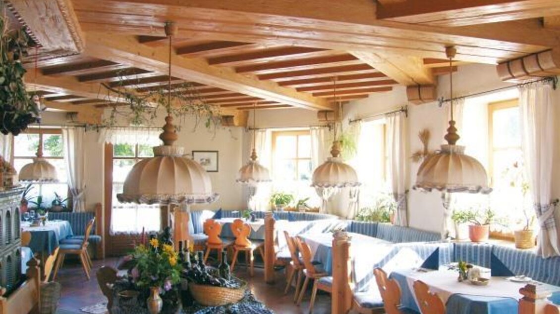 Ein einladendes Restaurant mit Holzdecke und hellen Lampen. Die Tische sind liebevoll gedeckt und von Pflanzen umgeben.