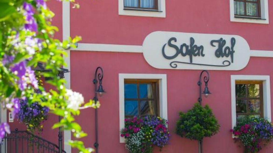 Ein charmantes, rosa Gebäude mit der Aufschrift "Sofaden Hof". Es ist von blühenden Pflanzen umgeben, die eine einladende Atmosphäre schaffen.