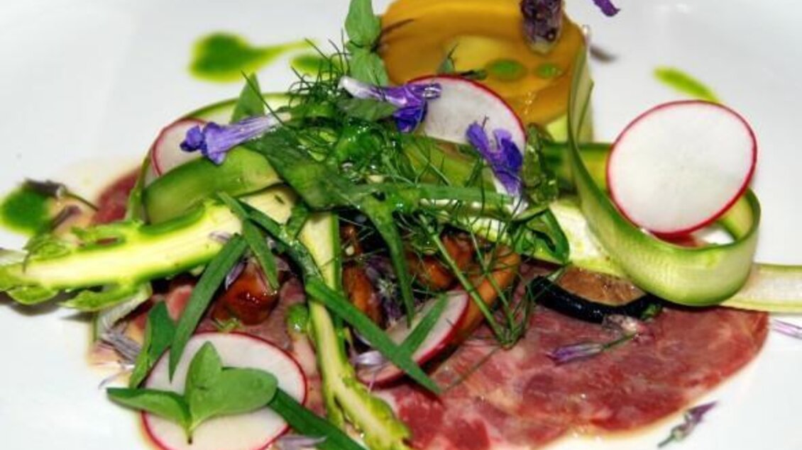 Ein kunstvoll angerichteter Teller mit Fleisch, frischem Gemüse und essbaren Blumen. Die farbenfrohen Zutaten bieten eine ansprechende Präsentation.