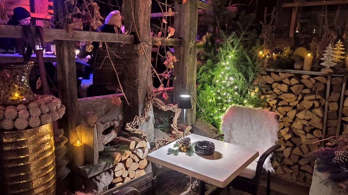 Eine gemütliche Sitzgelegenheit in einer festlich dekorierten Umgebung. Viele Holzstämme und Lichter schaffen eine warme, einladende Atmosphäre. | © Stocker Peter