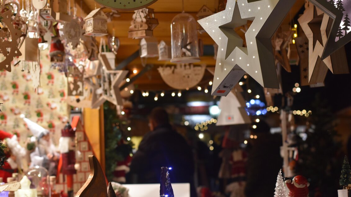 Ein stimmungsvolles Weihnachtsmarktstand mit leuchtenden Sternen und festlicher Dekoration. Im Hintergrund sind Menschen und Lichter zu sehen, die eine gemütliche Atmosphäre schaffen. | © Christian Thomaser
