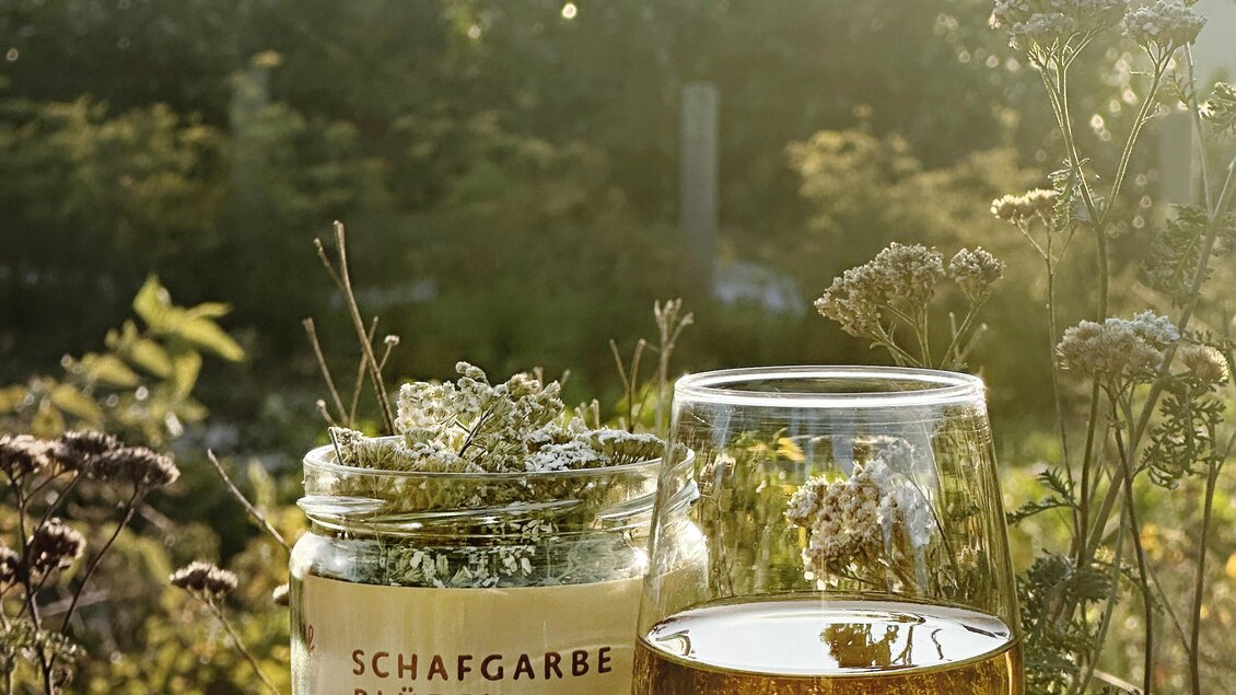 Glas mit Schafgarben-Tee und Kräuterblüten vom Lienhof in der Abendsonne der Steiermark | © Lienhof
