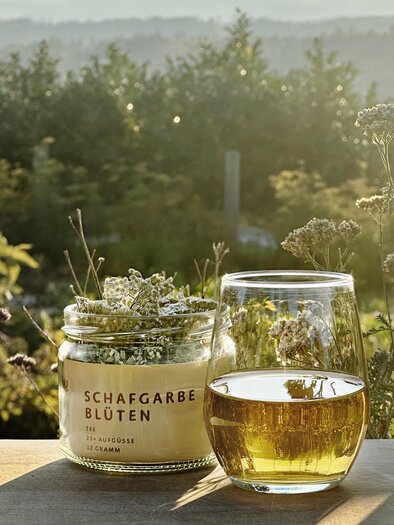 Glas mit Schafgarben-Tee und Kräuterblüten vom Lienhof in der Abendsonne der Steiermark | © Lienhof